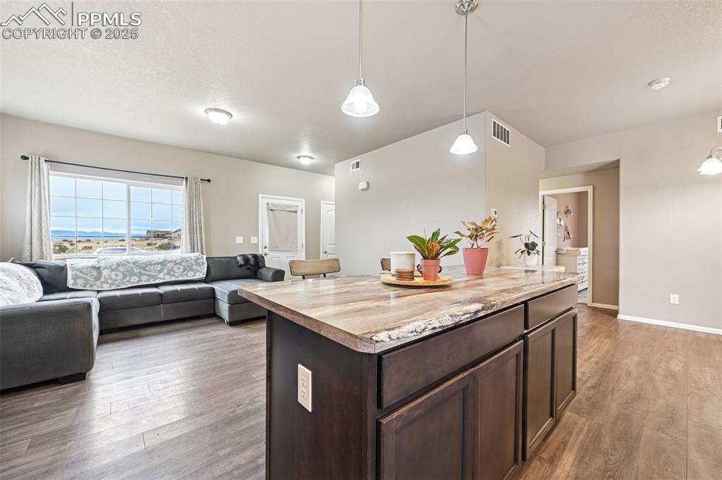 Kitchen featuring dark brown cabinetry, hanging light fixtures, open floor plan, a center island, and light wood finished floors