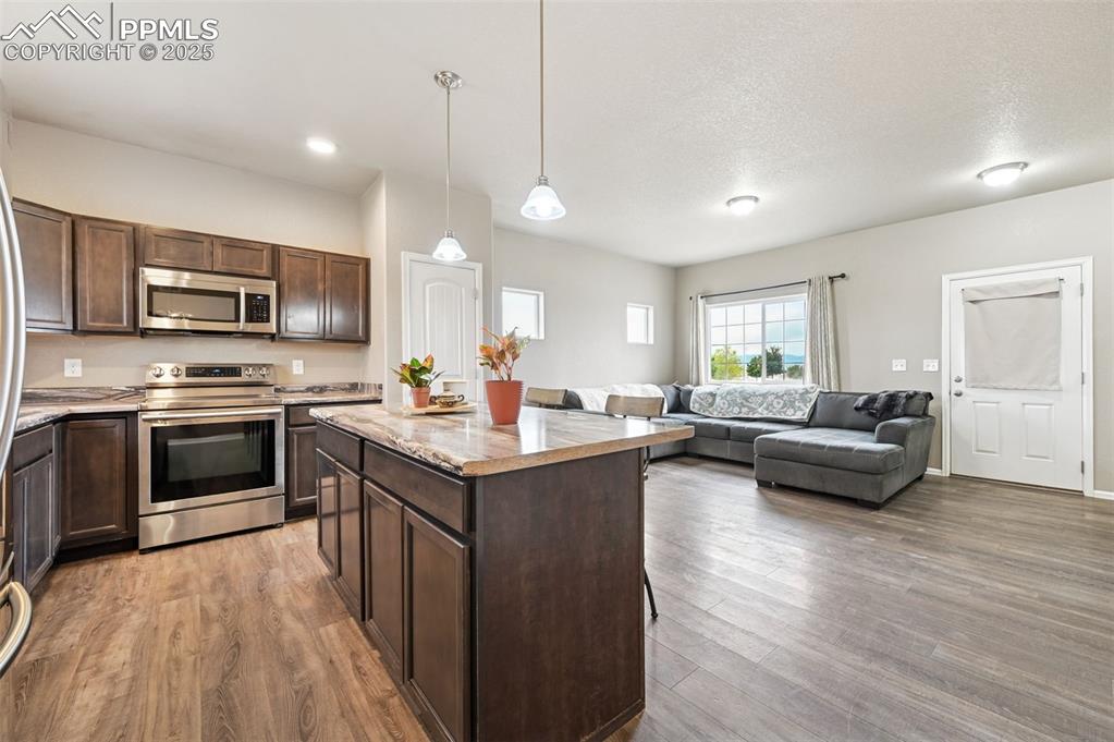 Kitchen featuring appliances with stainless steel finishes, a center island, dark brown cabinets, pendant lighting, and open floor plan