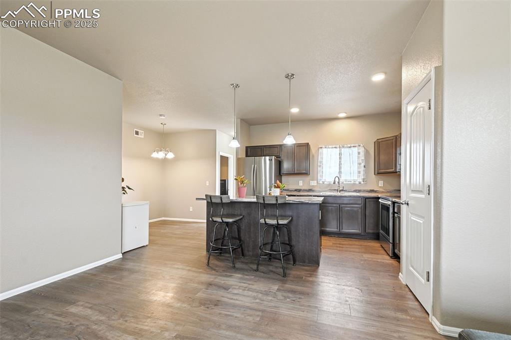 Kitchen featuring a kitchen island, a breakfast bar area, pendant lighting, appliances with stainless steel finishes, and light wood-style flooring