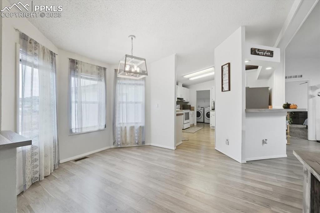 Unfurnished dining area with light wood finished floors, washing machine and dryer, a chandelier, and a textured ceiling
