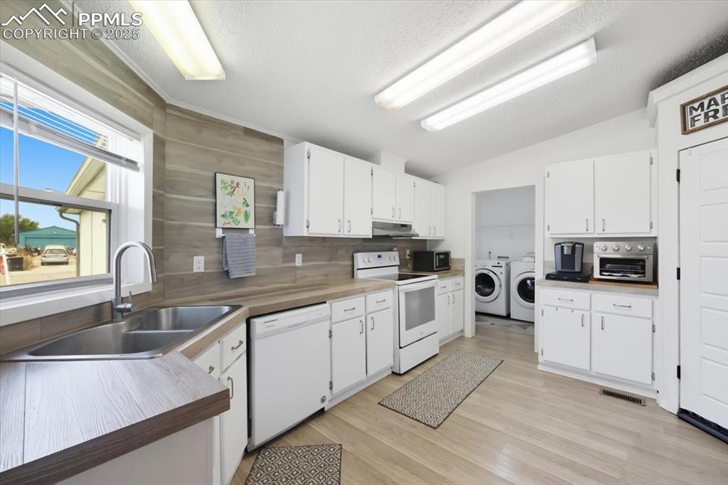 Kitchen with washing machine and clothes dryer, white appliances, white cabinetry, light wood-type flooring, and a textured ceiling