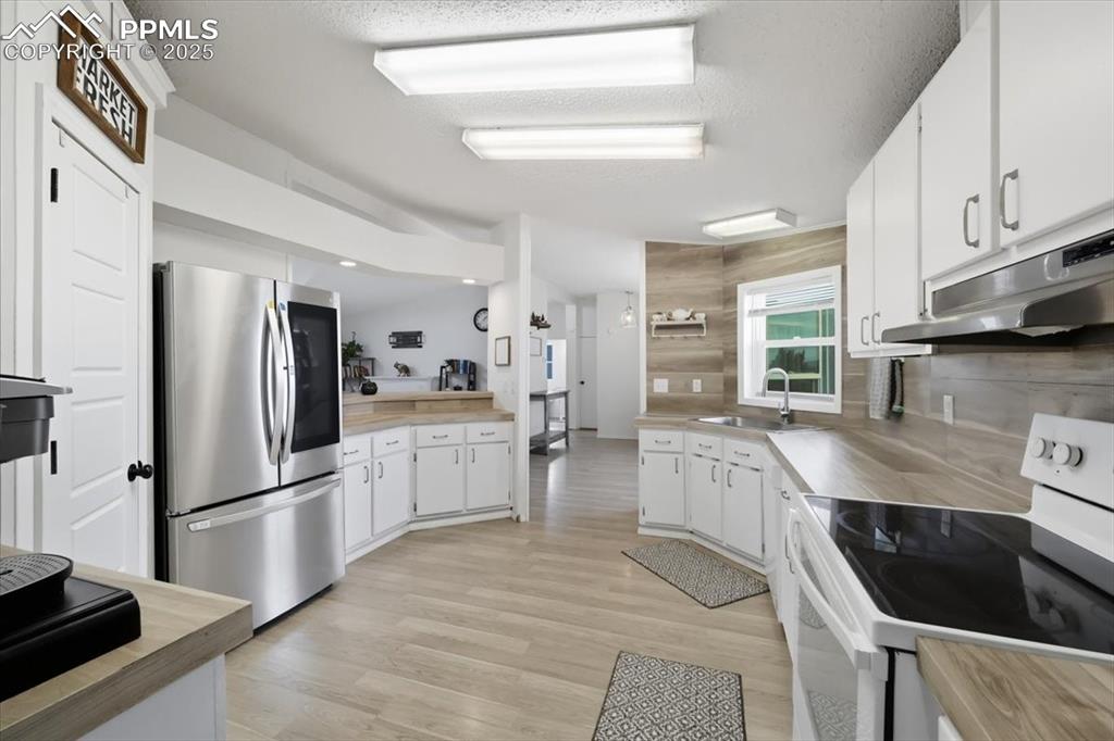 Kitchen with white range with electric stovetop, smart refrigerator, white cabinetry, light countertops, and a textured ceiling