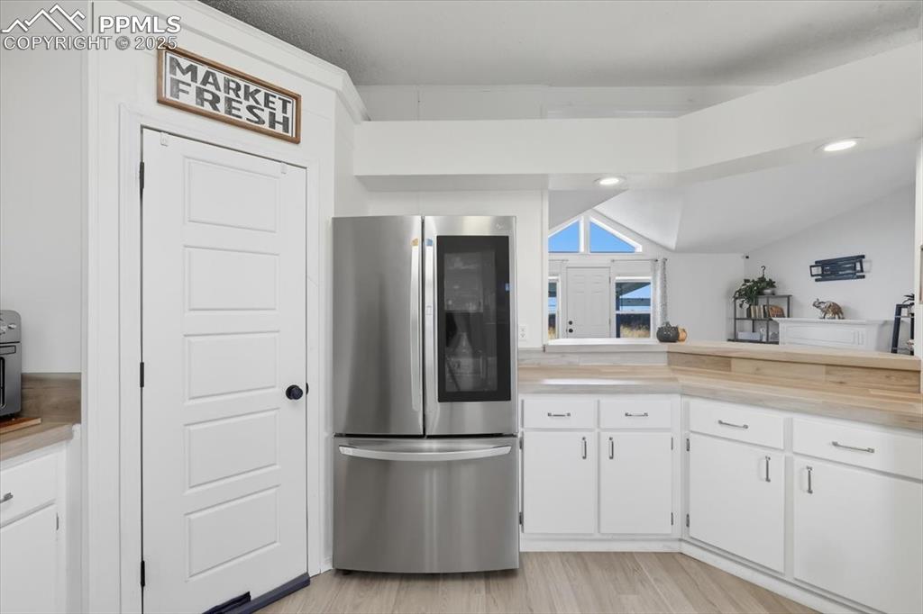 Kitchen with freestanding refrigerator, white cabinetry, light wood-type flooring, wood counters, and lofted ceiling