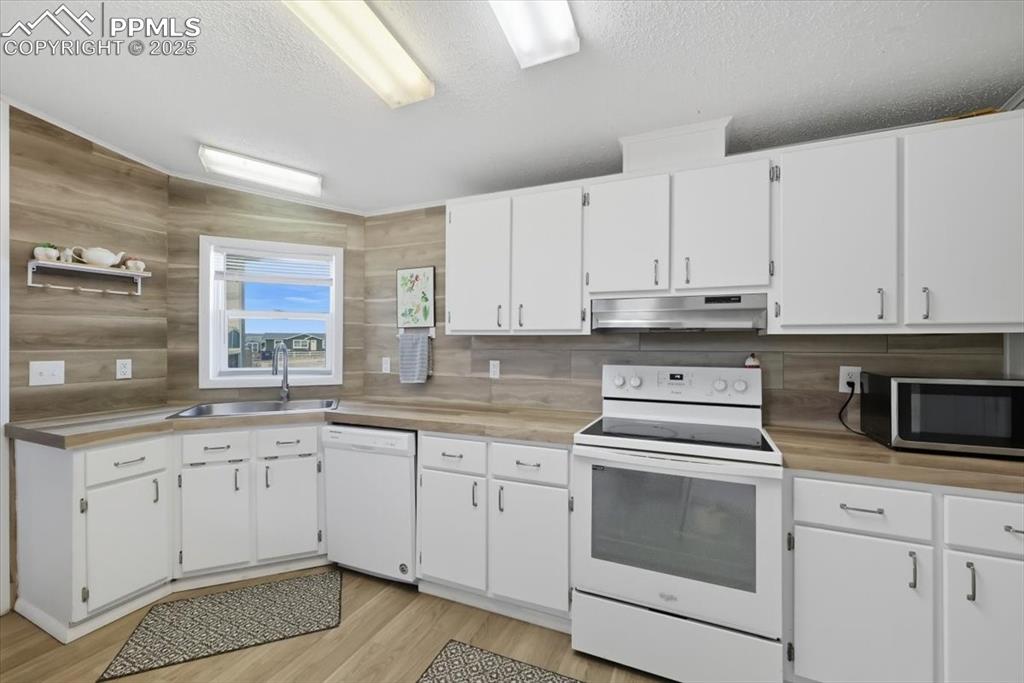 Kitchen with white cabinetry, white appliances, light countertops, a textured ceiling, and light wood finished floors