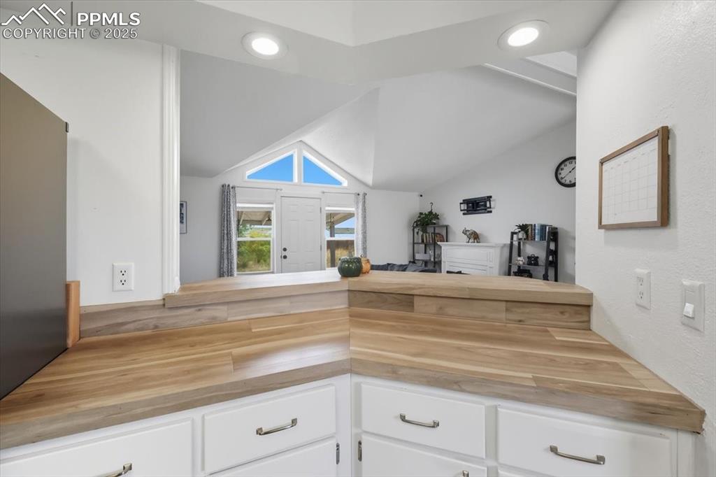 Kitchen featuring white cabinets, butcher block countertops, lofted ceiling, recessed lighting, and stainless steel fridge