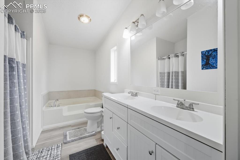 Bathroom featuring double vanity, a bath, light wood finished floors, and a shower with curtain