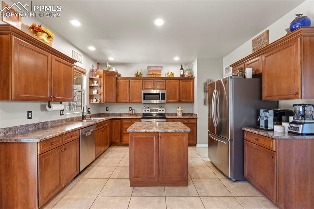 Kitchen featuring brown cabinets, open shelves, a kitchen island, appliances with stainless steel finishes, and light tile patterned floors
