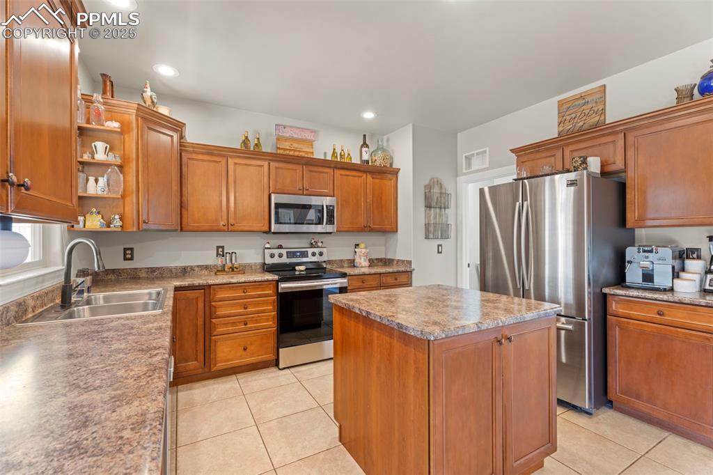 Kitchen with stainless steel appliances, brown cabinets, light tile patterned flooring, a kitchen island, and recessed lighting