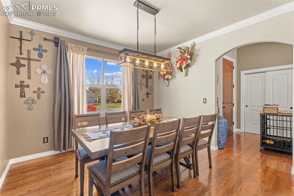 Dining room with crown molding, arched walkways, and light wood-type flooring