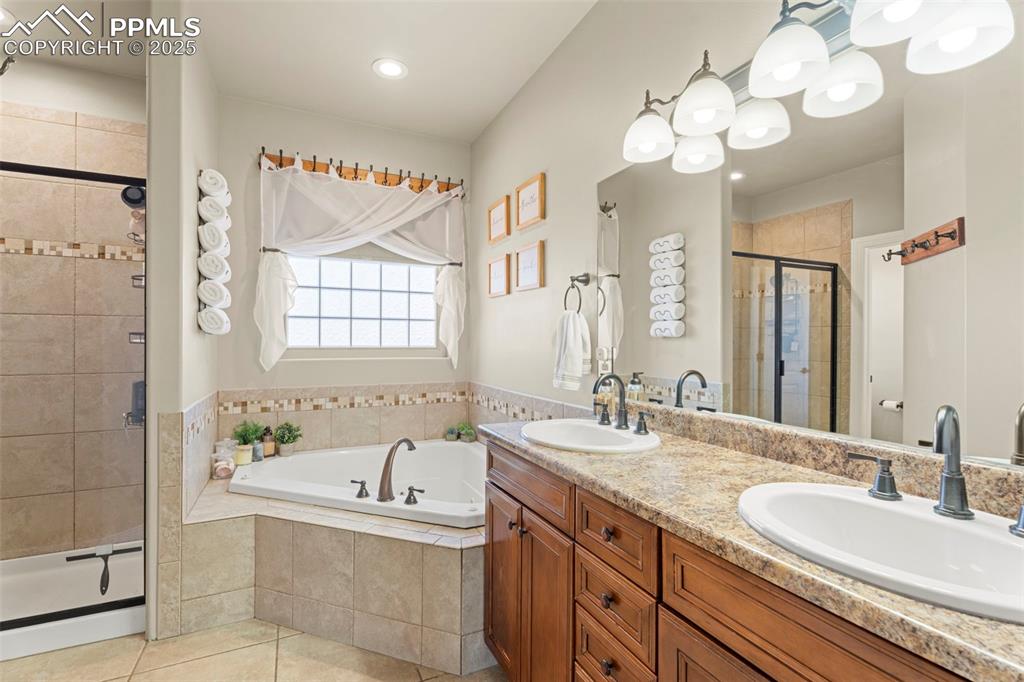 Full bathroom with double vanity, a bath, a stall shower, baseboard heating, and light tile patterned floors