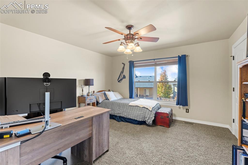 Carpeted bedroom with an office area and ceiling fan