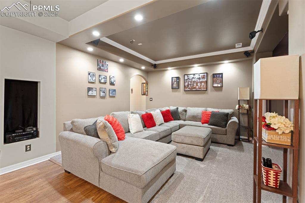 Living room with arched walkways, a raised ceiling, recessed lighting, light wood-style floors, and ornamental molding