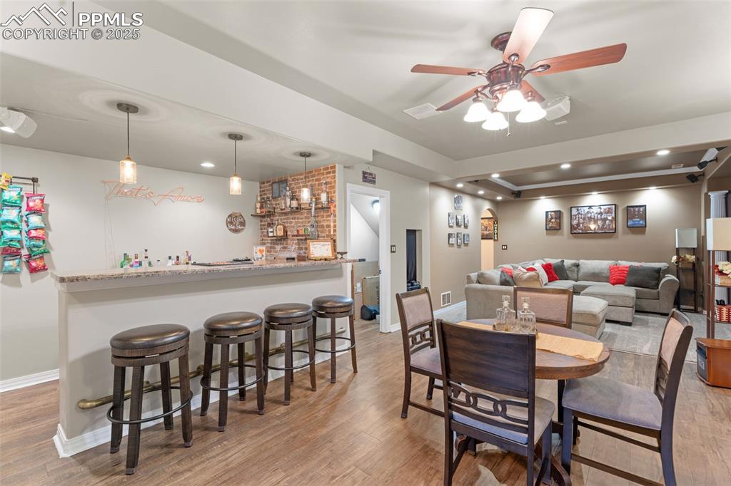 Dining space with light wood-style floors, bar, ceiling fan, a tray ceiling, and recessed lighting