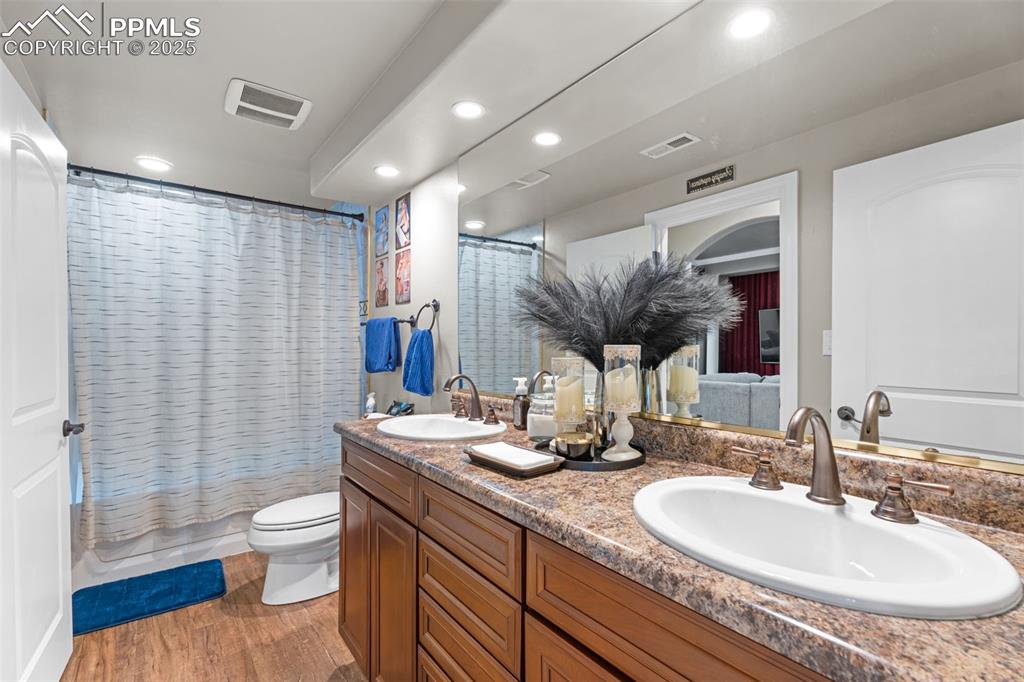 Full bathroom with double vanity, light wood-style flooring, shower / bathtub combination with curtain, recessed lighting, and connected bathroom