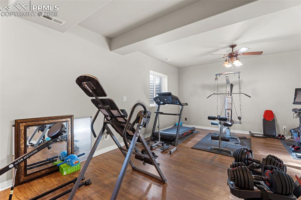 Exercise area featuring dark wood finished floors, ceiling fan, and beam ceiling