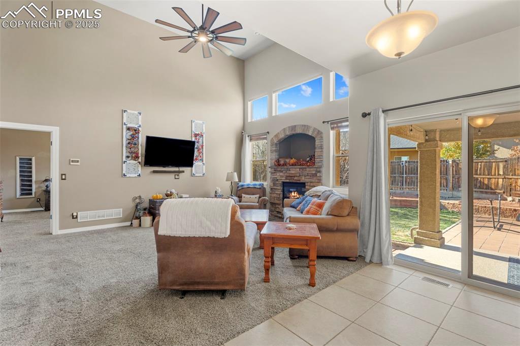 Carpeted living area featuring a towering ceiling, a fireplace, tile patterned floors, and ceiling fan