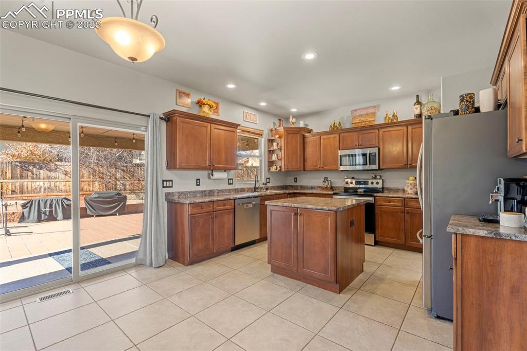 Kitchen with brown cabinets, stainless steel appliances, light tile patterned flooring, recessed lighting, and a center island