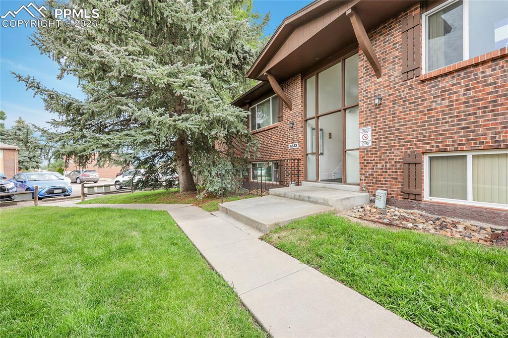 View of exterior entry with brick siding and a lawn
