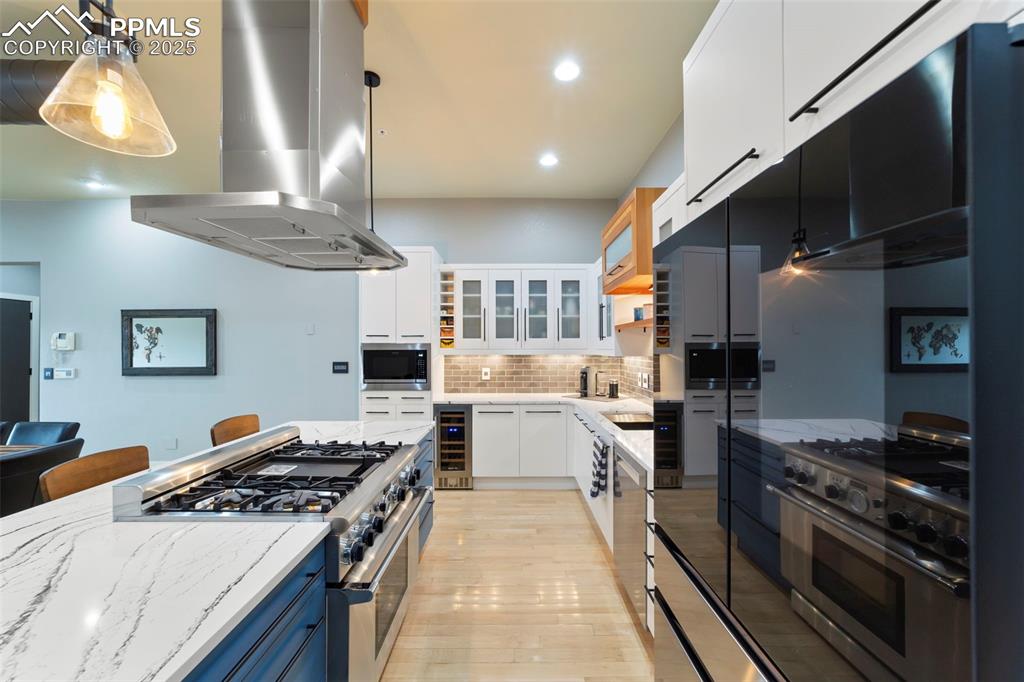 Kitchen with white cabinetry, Thermador range/oven with vent hood, stainless steel appliances, decorative backsplash, and glass insert cabinets