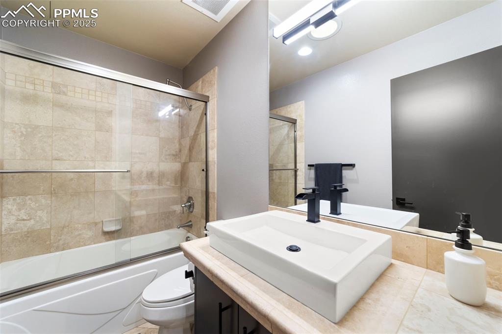 Full secondary bathroom featuring vanity and combined bath / shower with glass door