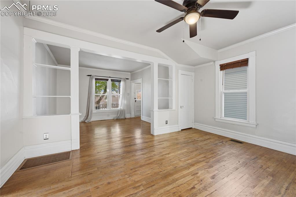 Empty room featuring light wood finished floors, crown molding, a ceiling fan, and built in features