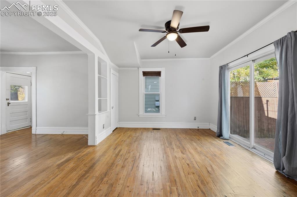 Empty room with plenty of natural light, ornamental molding, light wood-type flooring, and a ceiling fan
