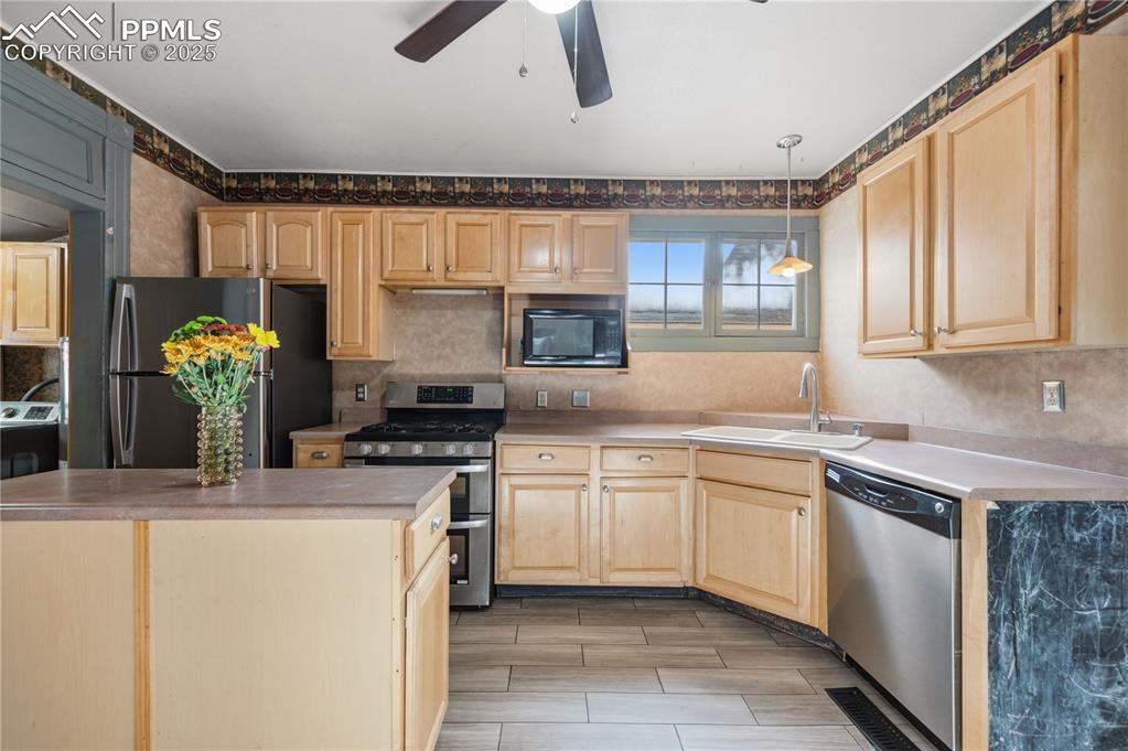 Kitchen with light brown cabinetry, appliances with stainless steel finishes, ceiling fan, and light countertops