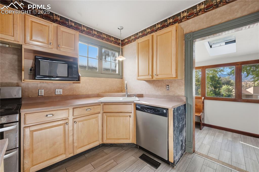 Kitchen featuring light brown cabinets, stainless steel appliances, decorative light fixtures, and healthy amount of natural light