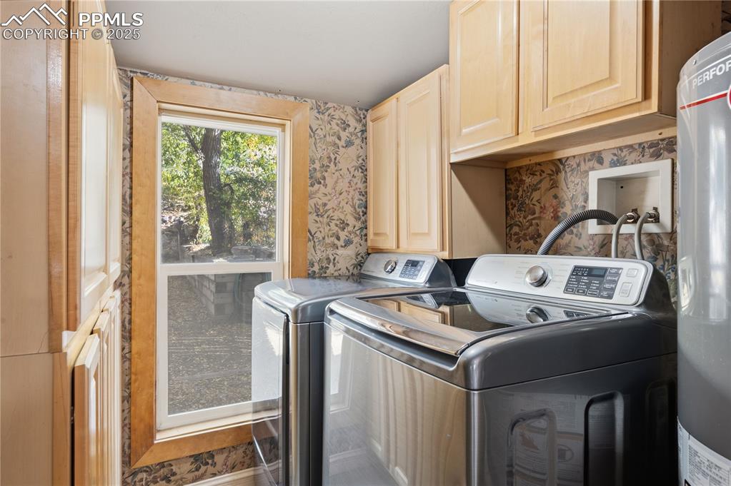 Laundry area featuring wallpapered walls, cabinet space, water heater, and washer and dryer