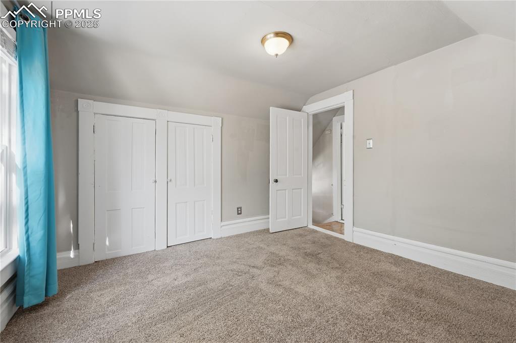 Unfurnished bedroom featuring vaulted ceiling, multiple windows, carpet, and a closet
