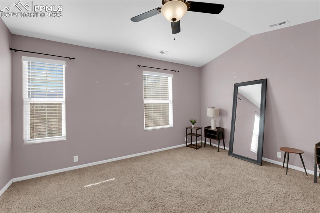 Primary bedroom with vaulted ceiling, ceiling fan, and light colored carpet