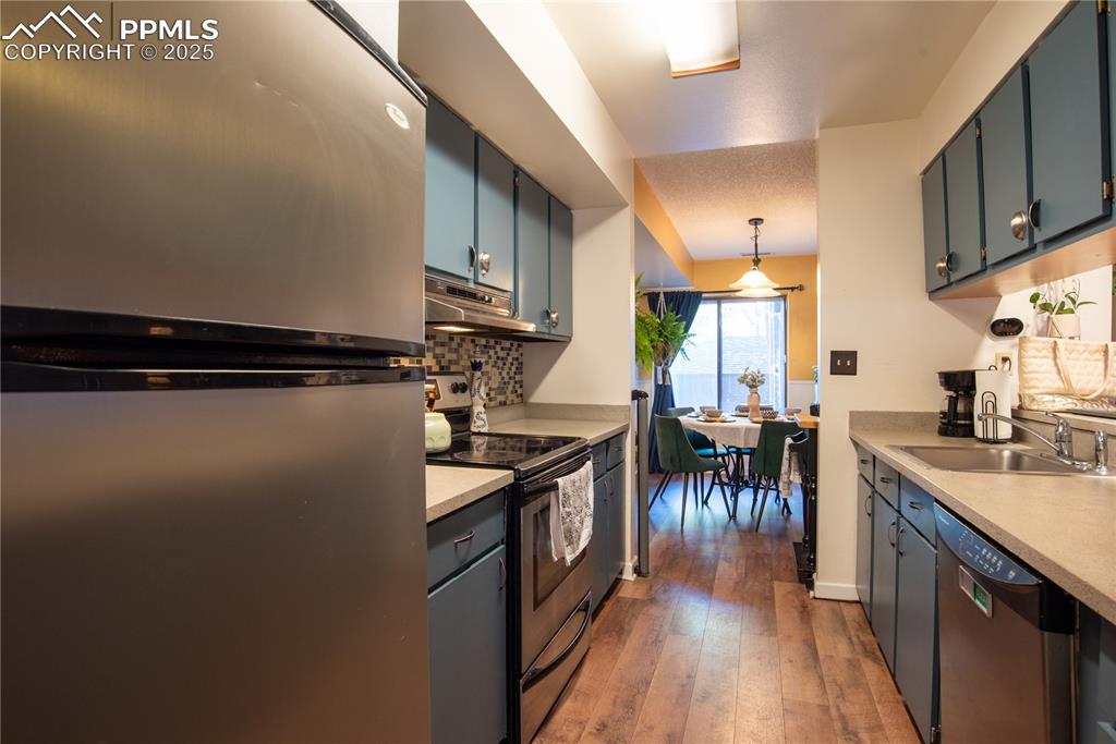 Kitchen with stainless steel appliances, backsplash, hanging light fixtures, light countertops, and light wood-style floors