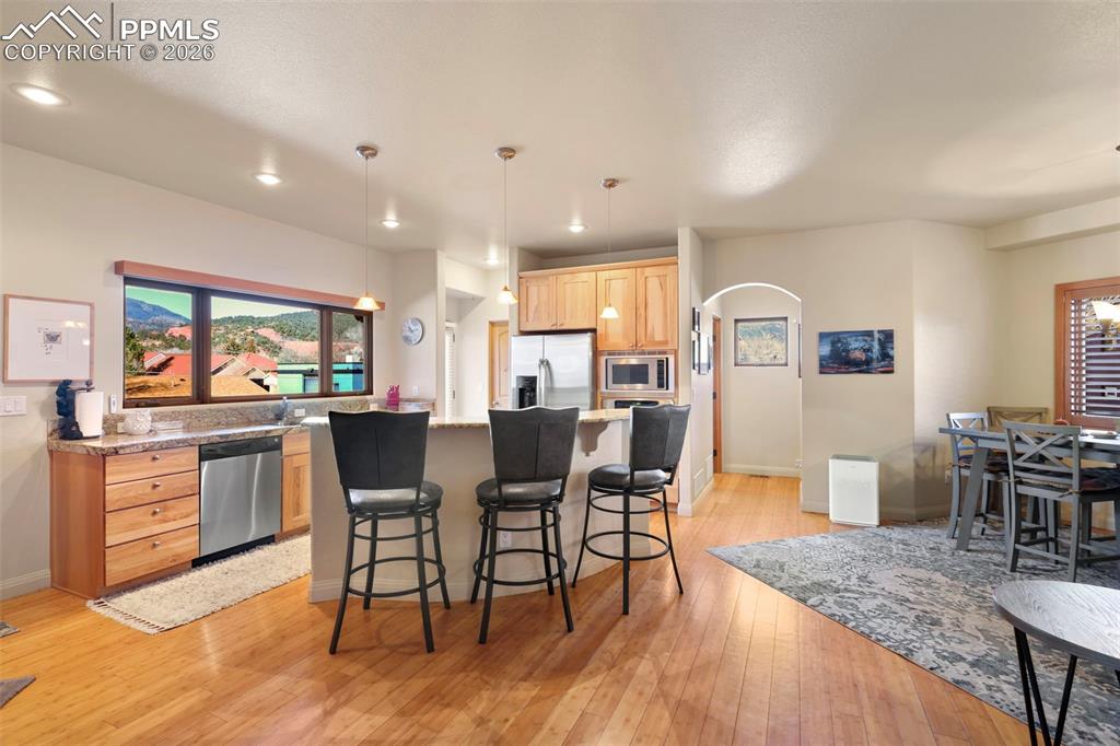 Kitchen featuring light wood finish cabinets, stainless steel appliances, light wood-style flooring, arched walkways, and a kitchen breakfast bar