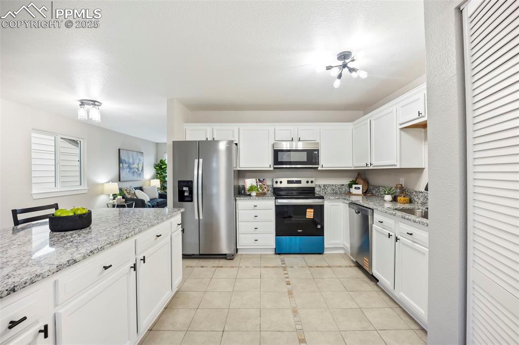 Kitchen featuring white cabinetry, appliances with stainless steel finishes, light stone counters, light tile patterned floors, and a textured ceiling