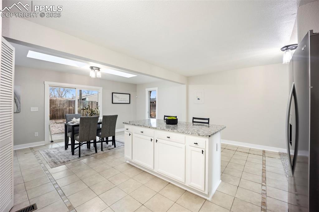 Kitchen with white cabinetry, stainless steel fridge, light stone countertops, and light tile patterned flooring