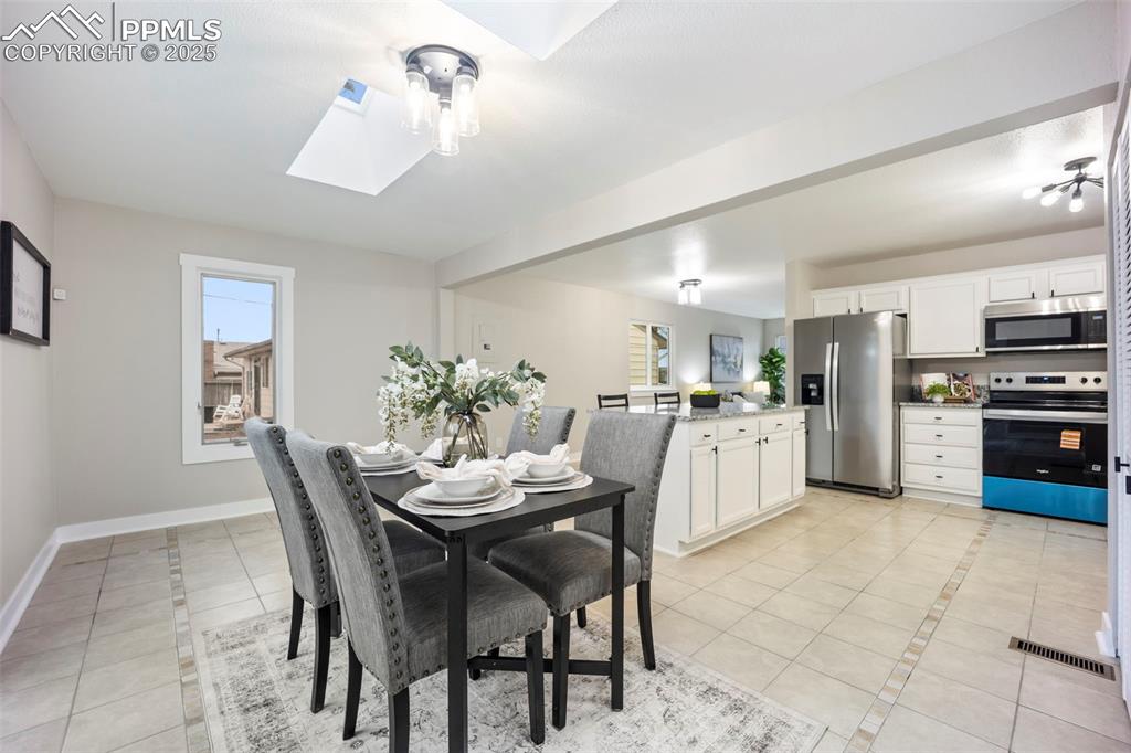Dining space featuring a skylight, light tile patterned floors, and inlaid floor details