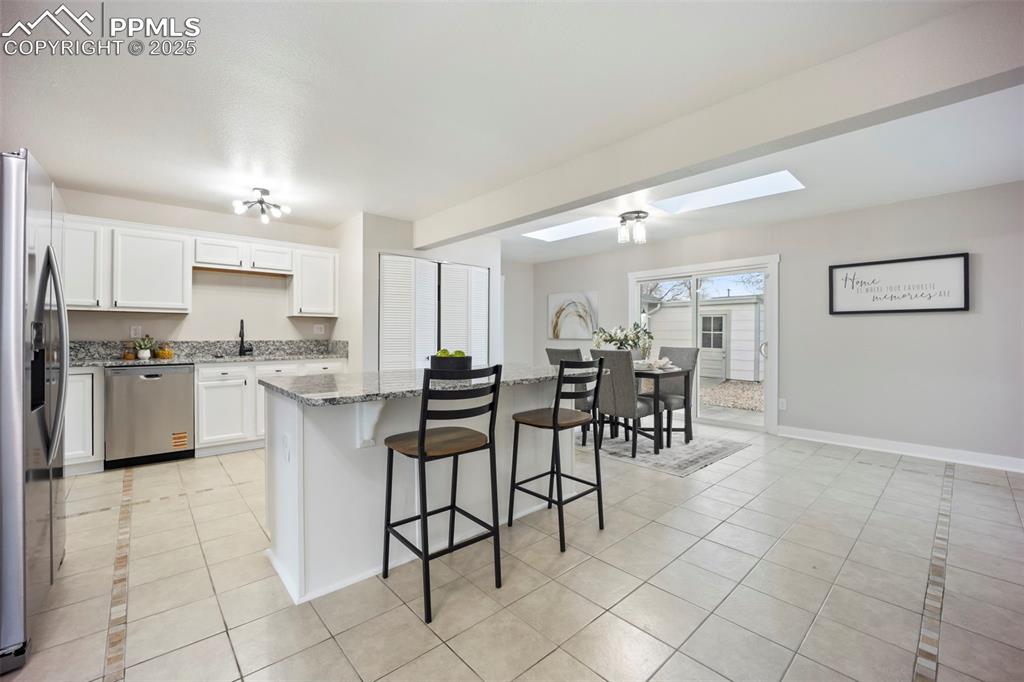 Kitchen with light tile patterned floors, a skylight, white cabinets, a breakfast bar, and stainless steel appliances