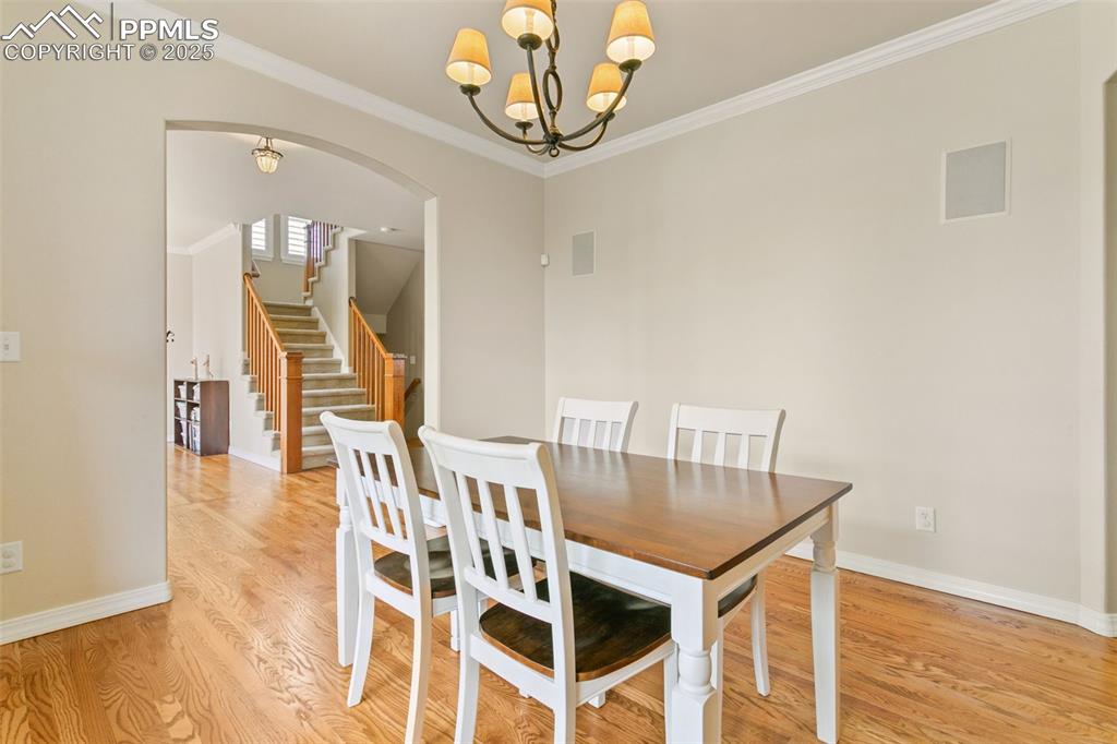 Dining room with crown molding, light wood finished floors, arched walkways, stairs, and a chandelier