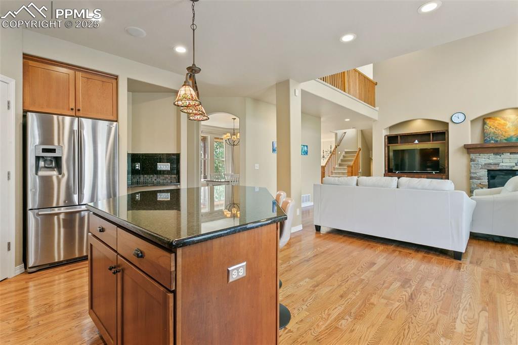Kitchen featuring brown cabinetry, dark stone countertops, stainless steel refrigerator with ice dispenser, recessed lighting, and a center island