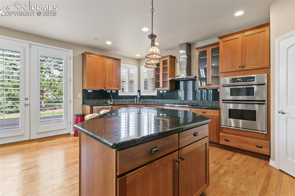 Kitchen featuring dark stone countertops, light wood-type flooring, a kitchen island, tasteful backsplash, and pendant lighting