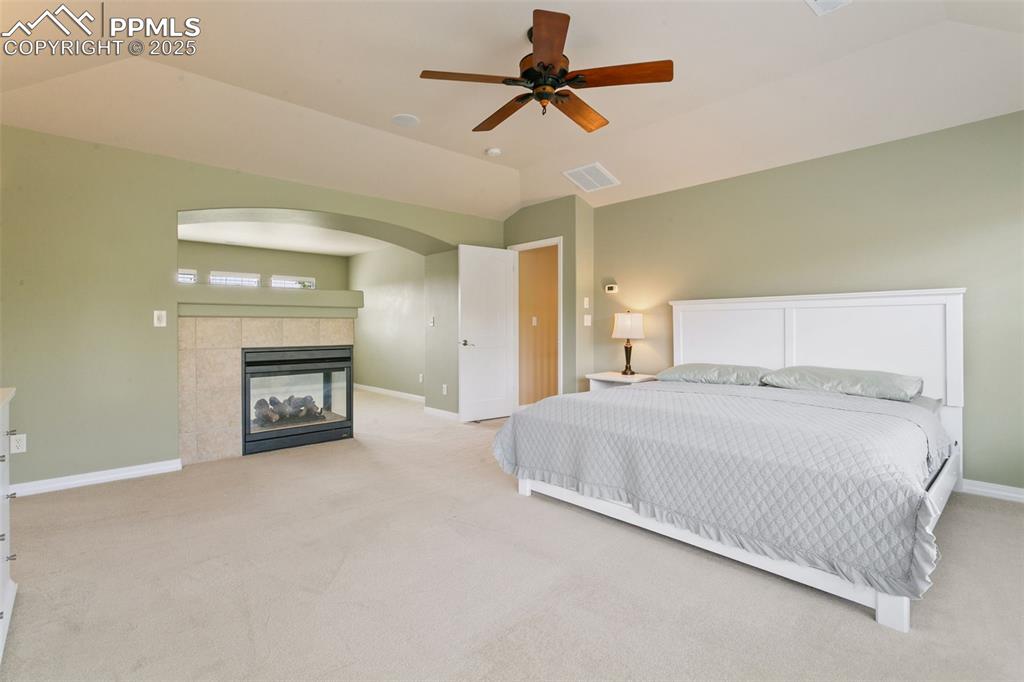 Bedroom with lofted ceiling, light colored carpet, a fireplace, and a ceiling fan