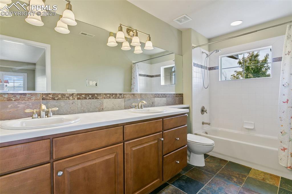 Bathroom featuring shower / bath combo, double vanity, and stone tile floors