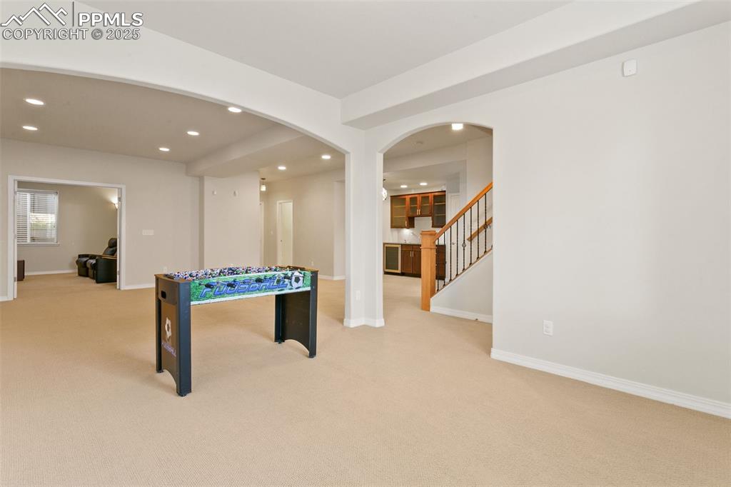 Recreation room with arched walkways, recessed lighting, and light carpet