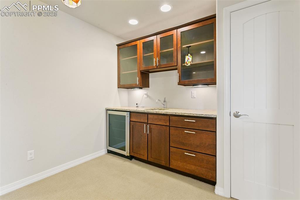 Indoor wet bar with glass insert cabinets, light carpet, beverage cooler, light stone countertops, and recessed lighting