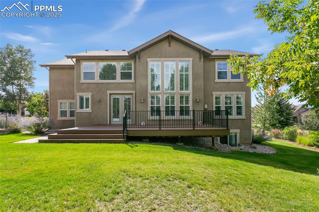 Back of house with a yard, stucco siding, a wooden deck, and french doors