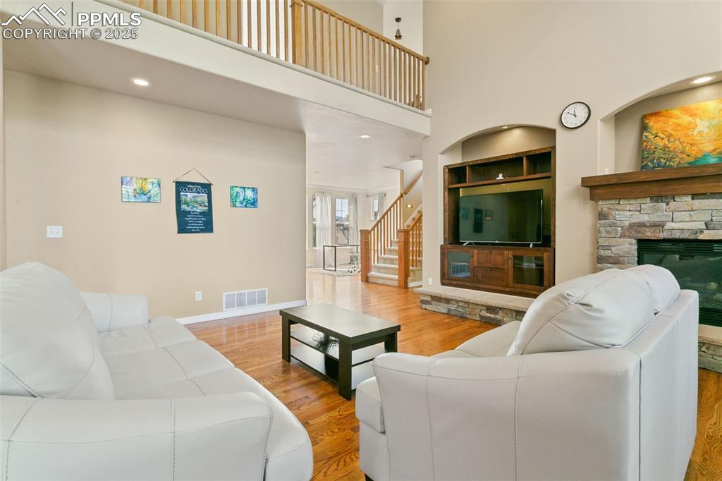 Living room with wood finished floors, stairway, a high ceiling, recessed lighting, and a fireplace
