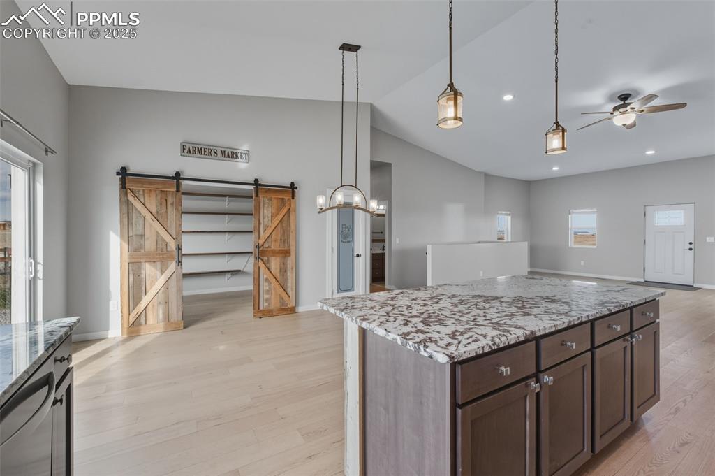 Kitchen featuring light stone counters, a barn door, hanging light fixtures, a center island, and light wood-style floors