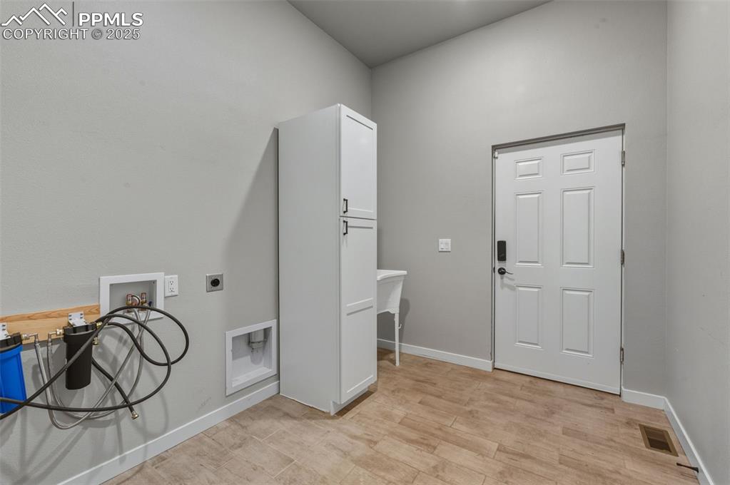 Washroom with hookup for an electric dryer, hookup for a washing machine, and light wood-style flooring