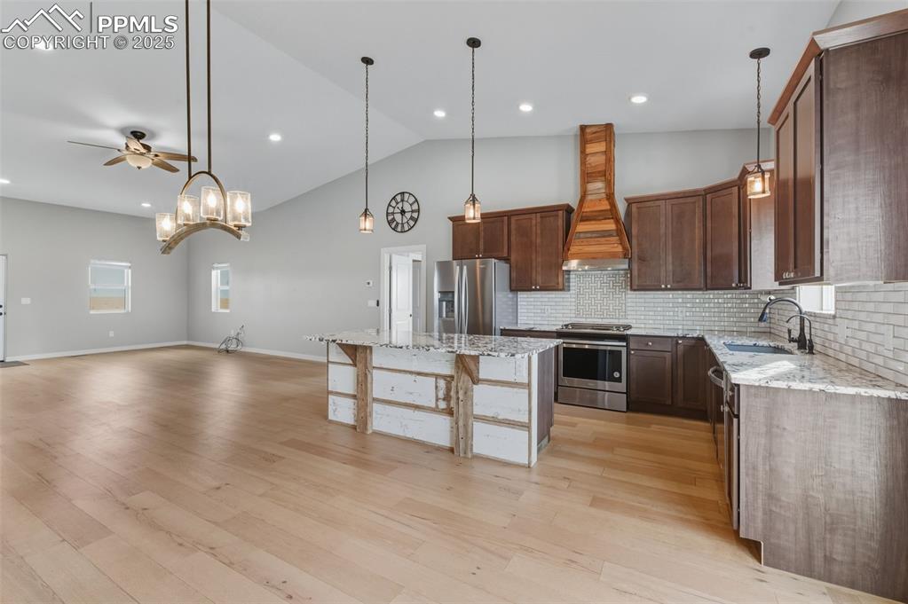 Kitchen featuring light stone countertops, hanging light fixtures, appliances with stainless steel finishes, custom exhaust hood, and recessed lighting