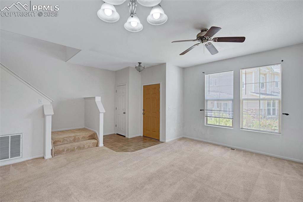 Unfurnished living room with carpet floors, stairway, and ceiling fan
